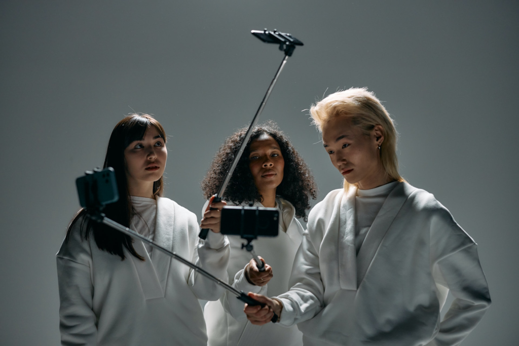 A group of three people taking individual selfies using selfie sticks